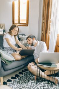 A young couple working together on laptops in a cozy living room setting, representing remote work.