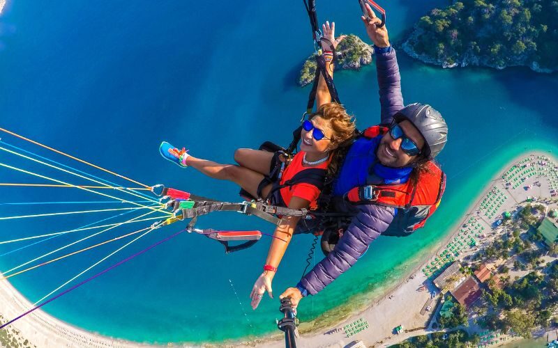 A woman and a man paragliding underneath of them a island of Ölüdeniz.