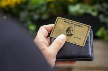 The American Express® Gold Card being held up in front of a bright blue wall
